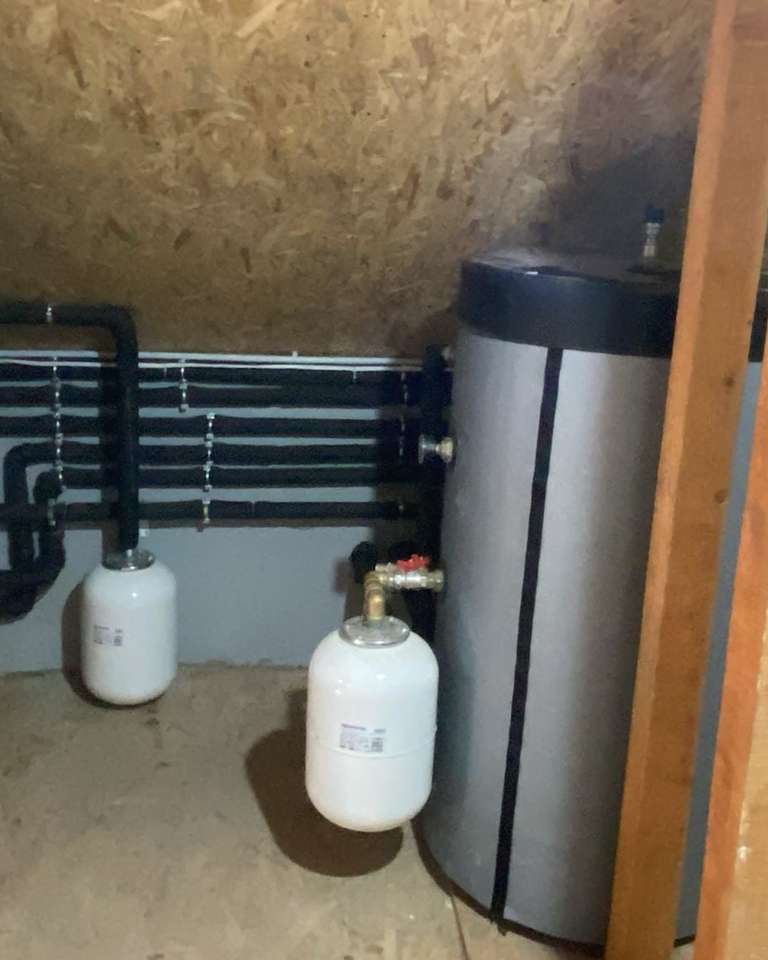 Cameră tehnică într-un pod, cu boiler, rezervor, vase de expansiune și țevi izolate negre