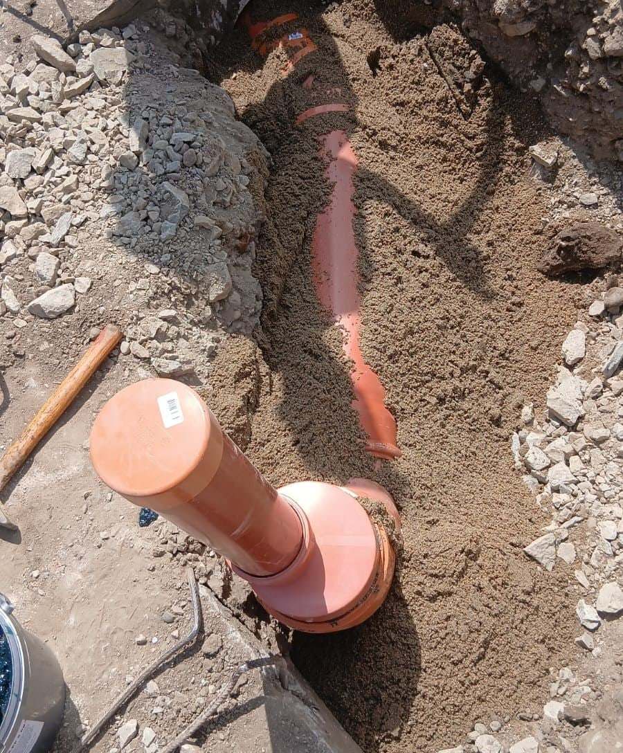 Țeavă portocalie de canalizare pe nisip, cu o piesă verticală de racord