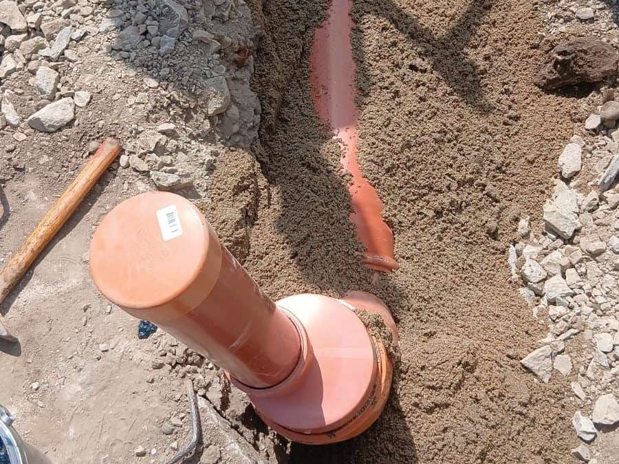 Țeavă portocalie de canalizare pe nisip, cu o piesă verticală de racord