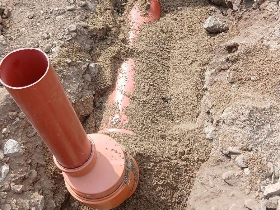 Țeavă portocalie de canalizare care trece pe sub fundația de beton, pozată pe nisip