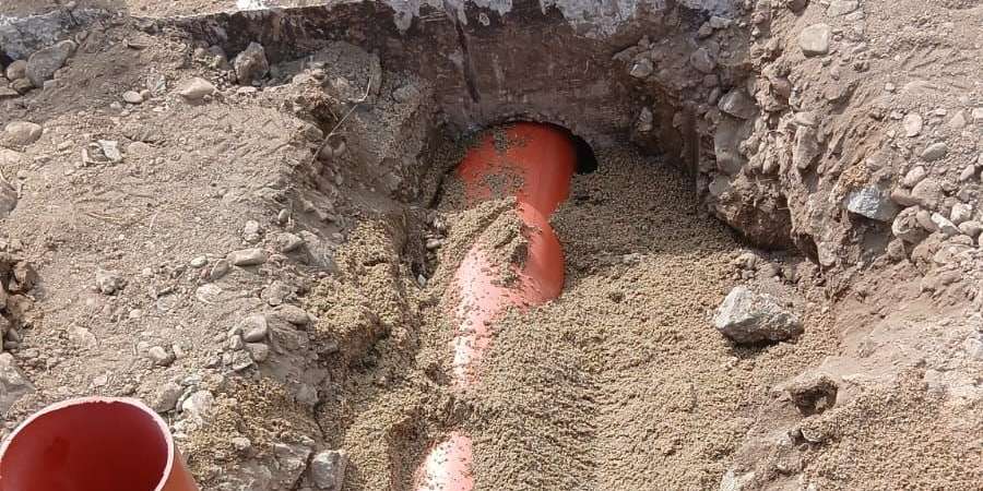 Țeavă portocalie de canalizare care trece pe sub fundația de beton, pozată pe nisip