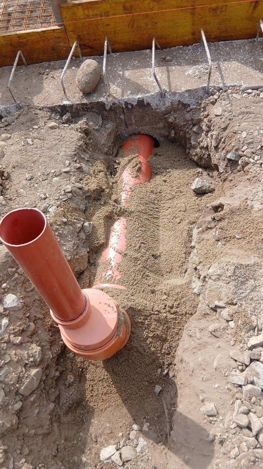 Țeavă portocalie de canalizare care trece pe sub fundația de beton, pozată pe nisip