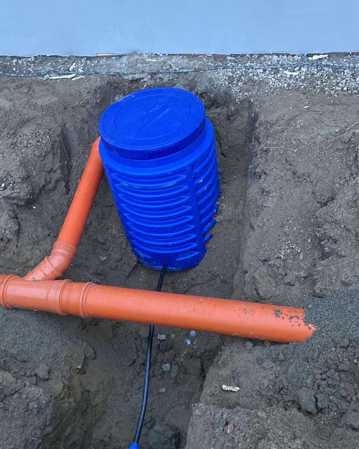 Cămin albastru de apometru într-o groapă, cu țeava portocalie de canalizare și conducta neagră de apă